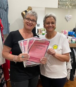 Two women wearing black and white holding four One Light Charity Foundation makeover certificates