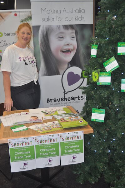 One Light Charity image of a young woman working for brave hearts standing behind a table raising funds for children who are abused at the Bartercard Shopfestival