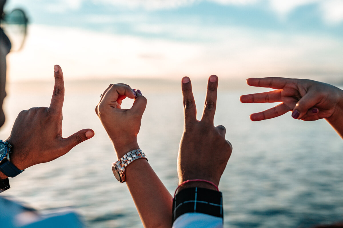 Image of hands spelling the word love with sea view in the background