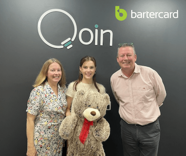 Two ladies with big teddy bear and man infront of Qoin and Bartercard logos
