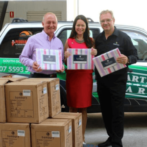 Image of staff at a Bartercard company car giving boxes of bedding to a lady representing GIVIT
