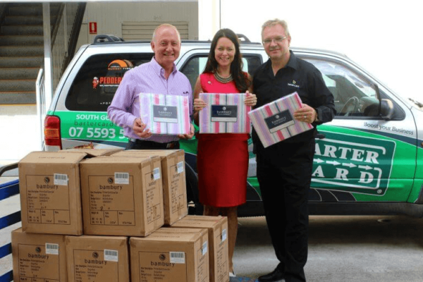 Image of staff at a Bartercard company car giving boxes of bedding to a lady representing GIVIT