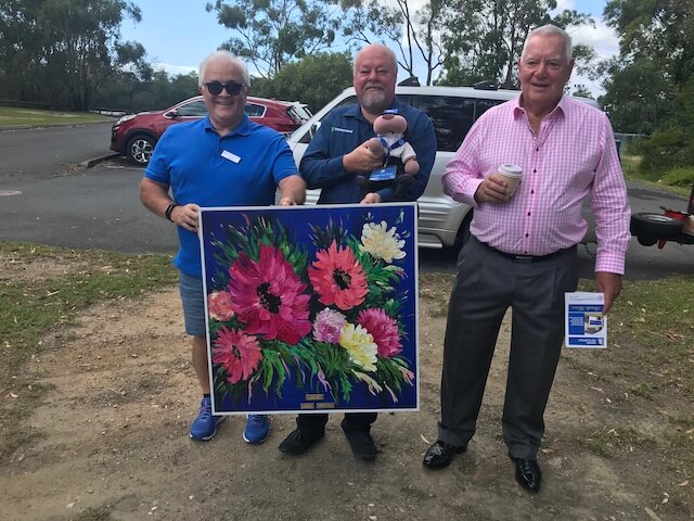 Three men standing infront of flower painting donated by One Light Charity