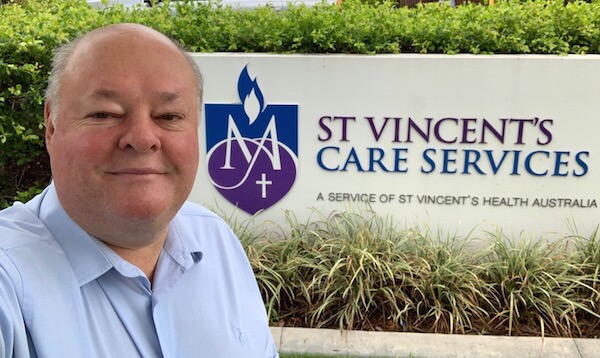 Image of One Light Charity Director, Tony Wiese in front of Vinnies Care Services logo