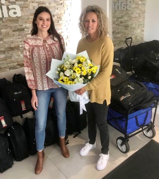 Two ladies standing next to each other, one is holding a bunch of yellow flowers