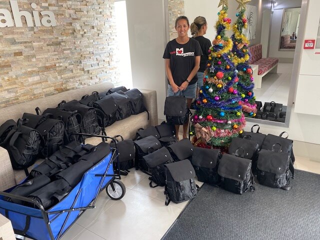 Lady standing next to Christmas tree surrounded with black backpacks