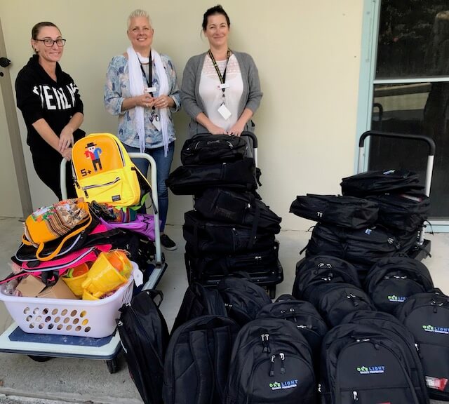 Three ladies behind One Light Charity backpack donation