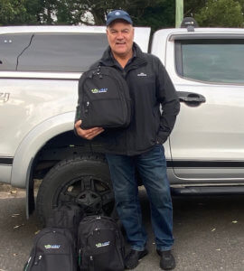 Man standing infront of silver ute with One Light Charity backpacks