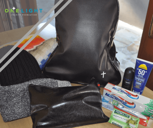 Image of a black backpack with clothing and personal hygiene items on display for the One Light Charity backpack Campaign for the homeless.