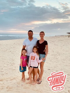 Beach photo of a family with two little girls smiling looking happy