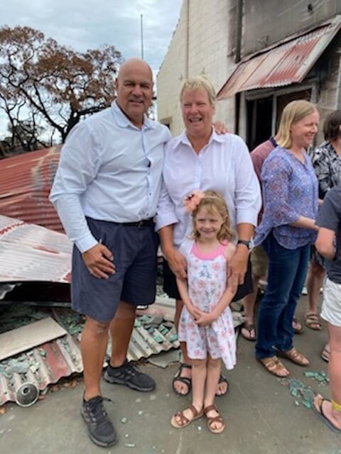 One Light Charity's Director standing with people of the Stokes Bay Community next to the hall burned down by the bushfires