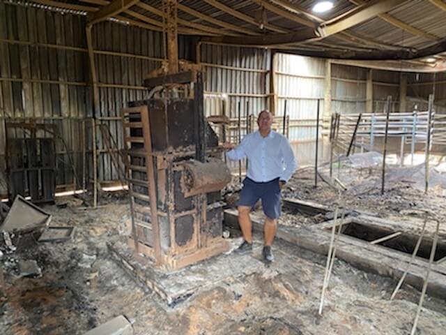 Man in blue shirt and shorts standing in a burnt down wool shed
